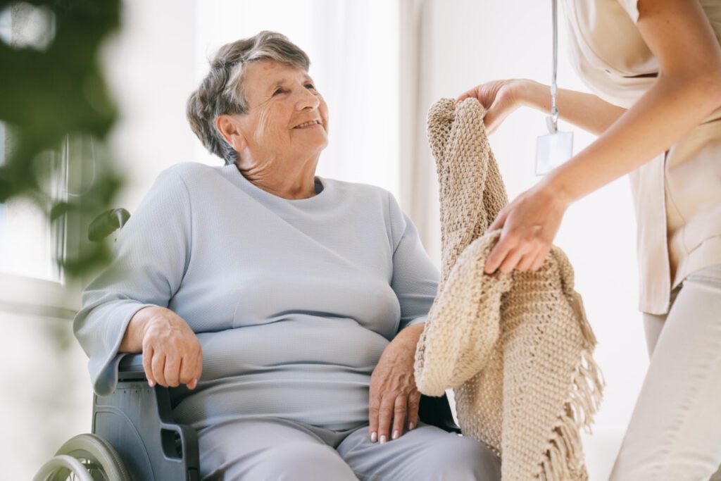 vrijwilliger geeft een dekentje aan een vrouw in een rolstoel - Hospice-info